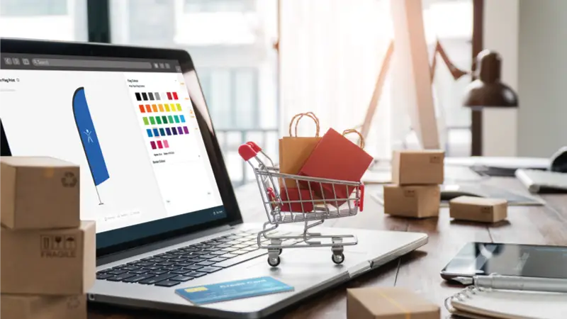 Laptop with small cart on keyboard to show ecommerce shopping. Monitor shows a product being ordered on the Kit Builder 3D Customizer interface. 3D customization with ecommerce integration.